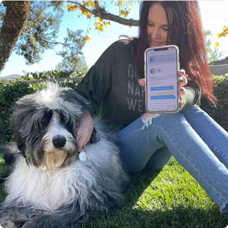 A woman with her dog holds a phone showing her pet's online profile.
